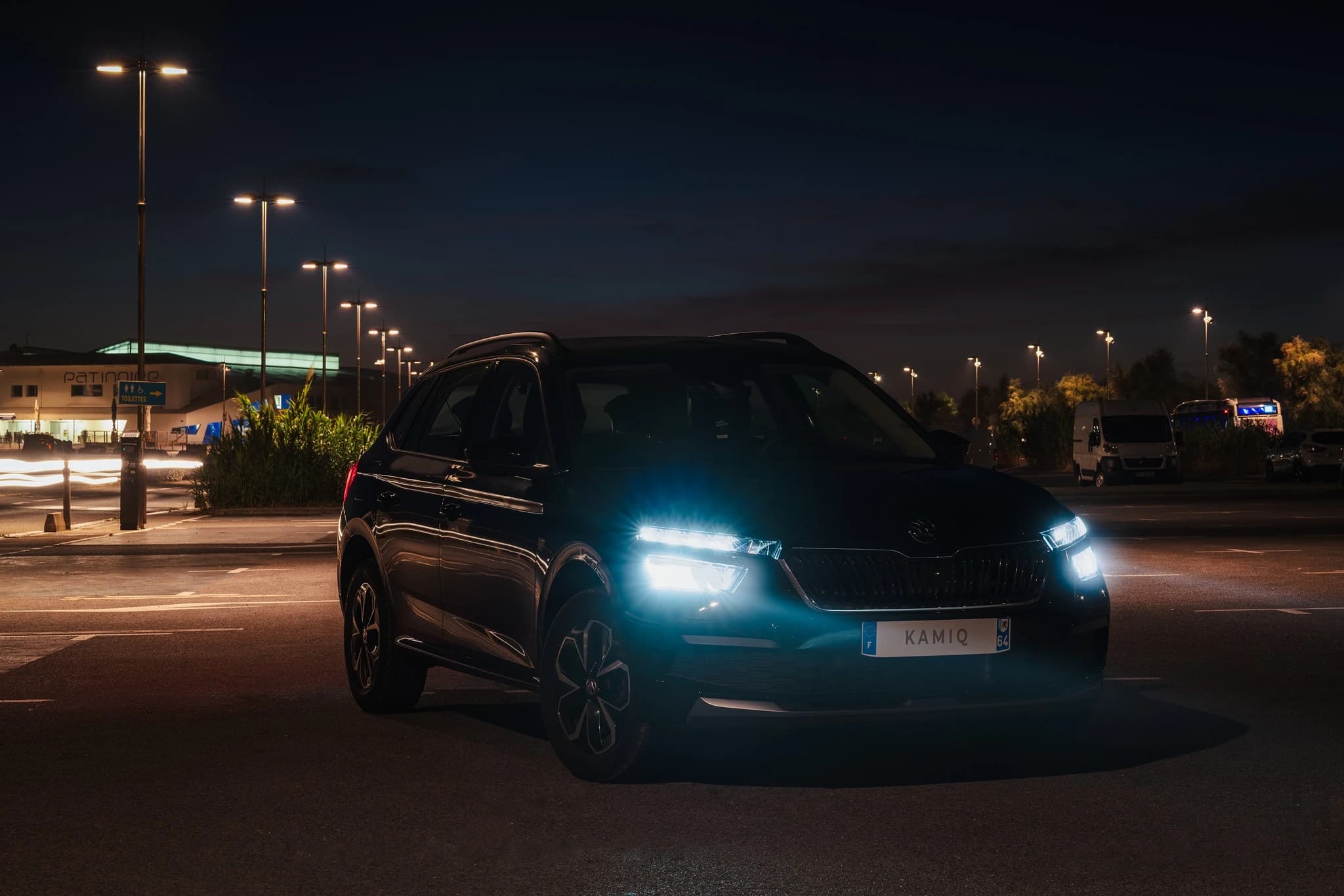 Skoda Kamiq de trois quarts à la nuit tombée, sous les lampadaires, phares allumés.