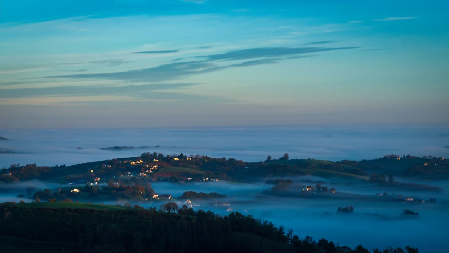 Collines et habitations baignées de brume bleue.